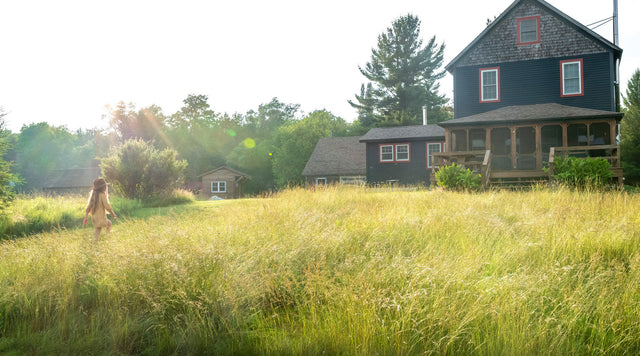 young girl walking through grassy meadow in front of house