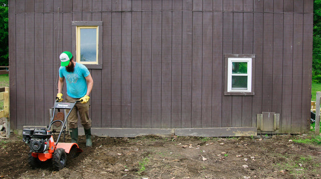 Man rototilling in front of wooden shed