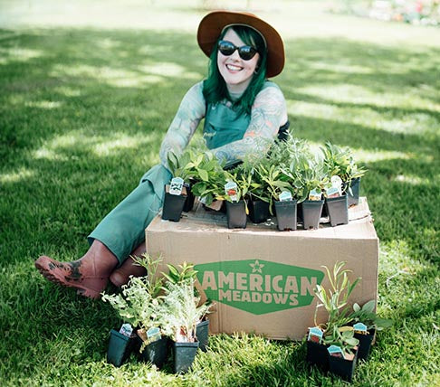 Woman sitting on a lawn surrounded by American Meadows plant products